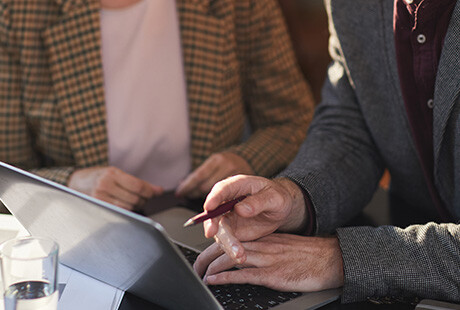 en person använder en laptop, en person sitter bredvid, bilden är skuren i axelhöjd