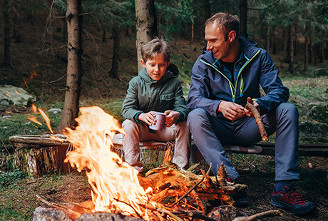 pappa och son sitter vid en brasa i skogen