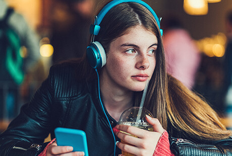 tjej lyssnar i hörlurar, håller i sin mobil och en smoothie