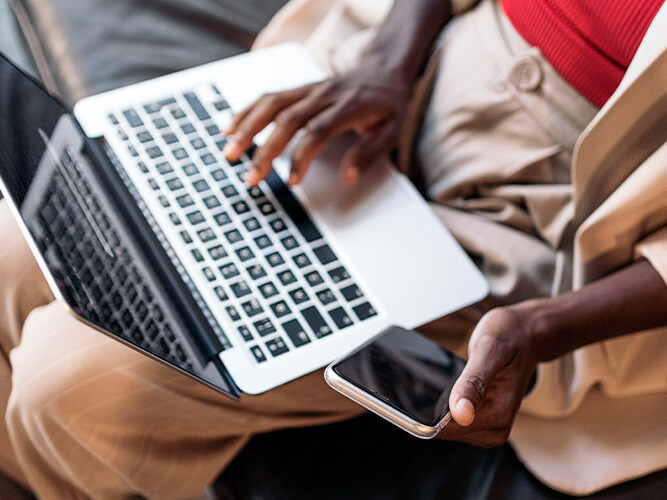 person som sitter med en laptop i knäet och en mobil i handen