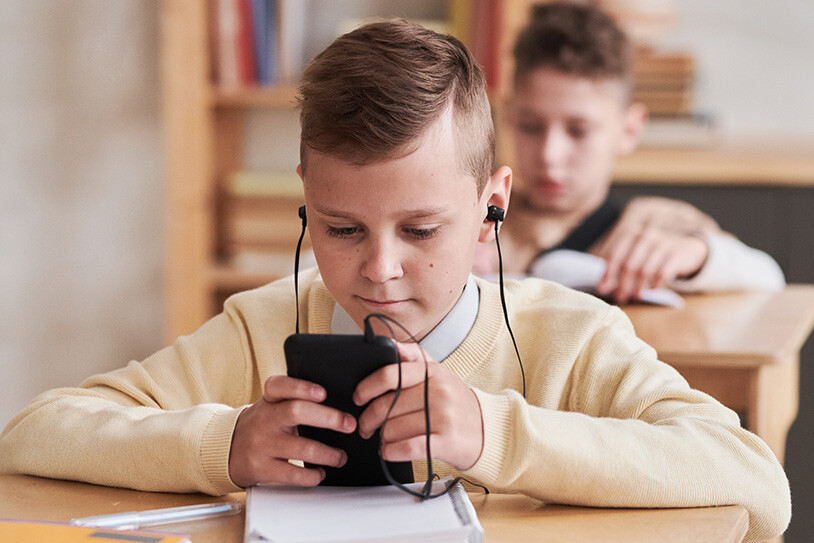 pojke sitter i klassrum med sin mobil och hörlurar i öronen