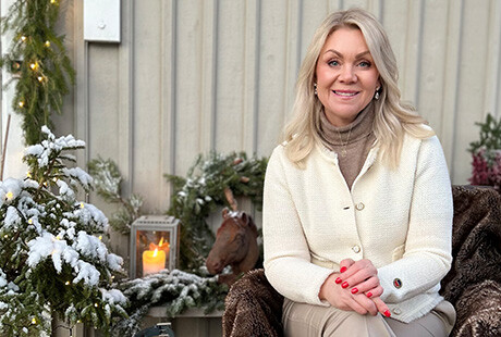 VD Sofia Skog sitter utomhus vid en husvägg. Tänd lykta och granris med snö på syns på bilden. 